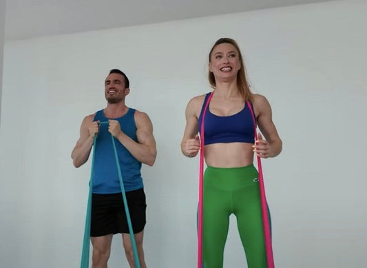 Kadın ve erkek sporcu direnç bandı ile front squat yapıyor – evde bacak ve kalça kaslarını çalıştıran etkili egzersiz. | Female and male athletes doing resistance band front squats – a powerful home workout for legs and glutes.