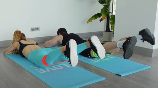 Kadın ve erkek yüzüstü pozisyonda direnç bandıyla prone leg raise egzersizi yapıyor | Man and woman performing resistance band prone leg raise exercise.